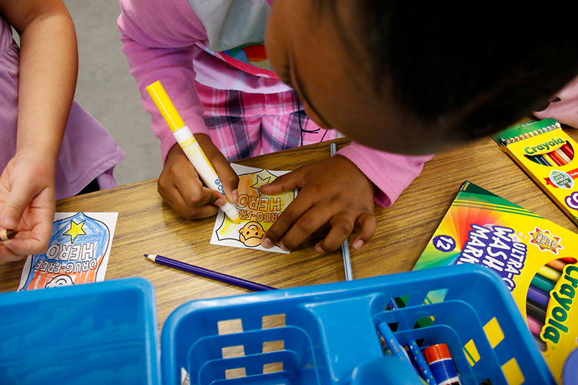 A girl colors a piece of paper with Drug Free Hero printed on it