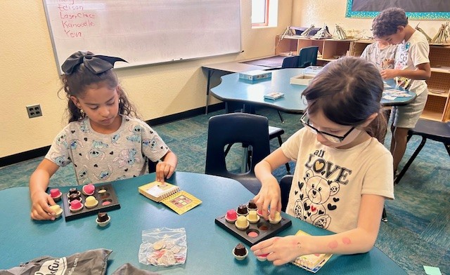 This picture shows students participating in a logic-based activity arranging plastic chocolate pieces as part of our Olympics of the Mind unit, engaging with one of Gardner’s multiple intelligences.