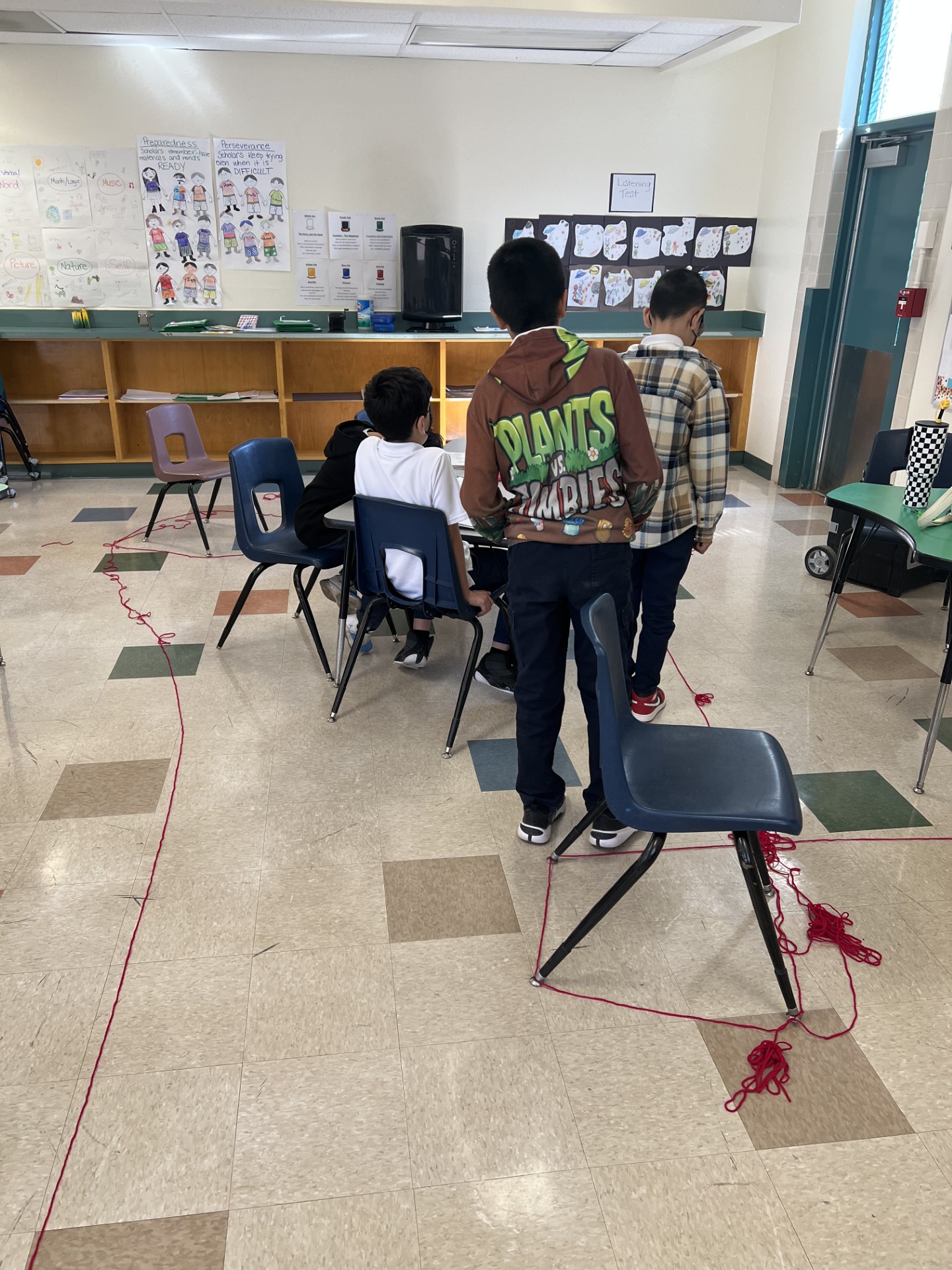 Image shows students standing around a table and yarn unraveled on the floor around them.