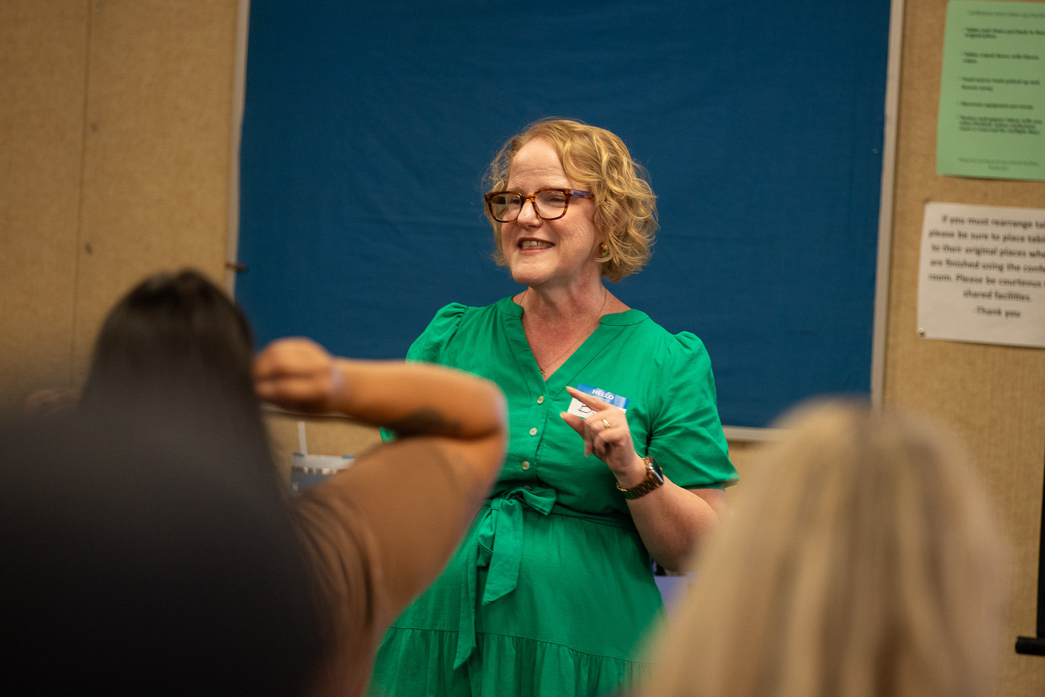 A woman wearing green and glasses addresses the group