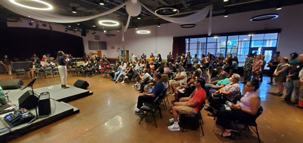 A speaker stands facing a seated crowd listening intently.