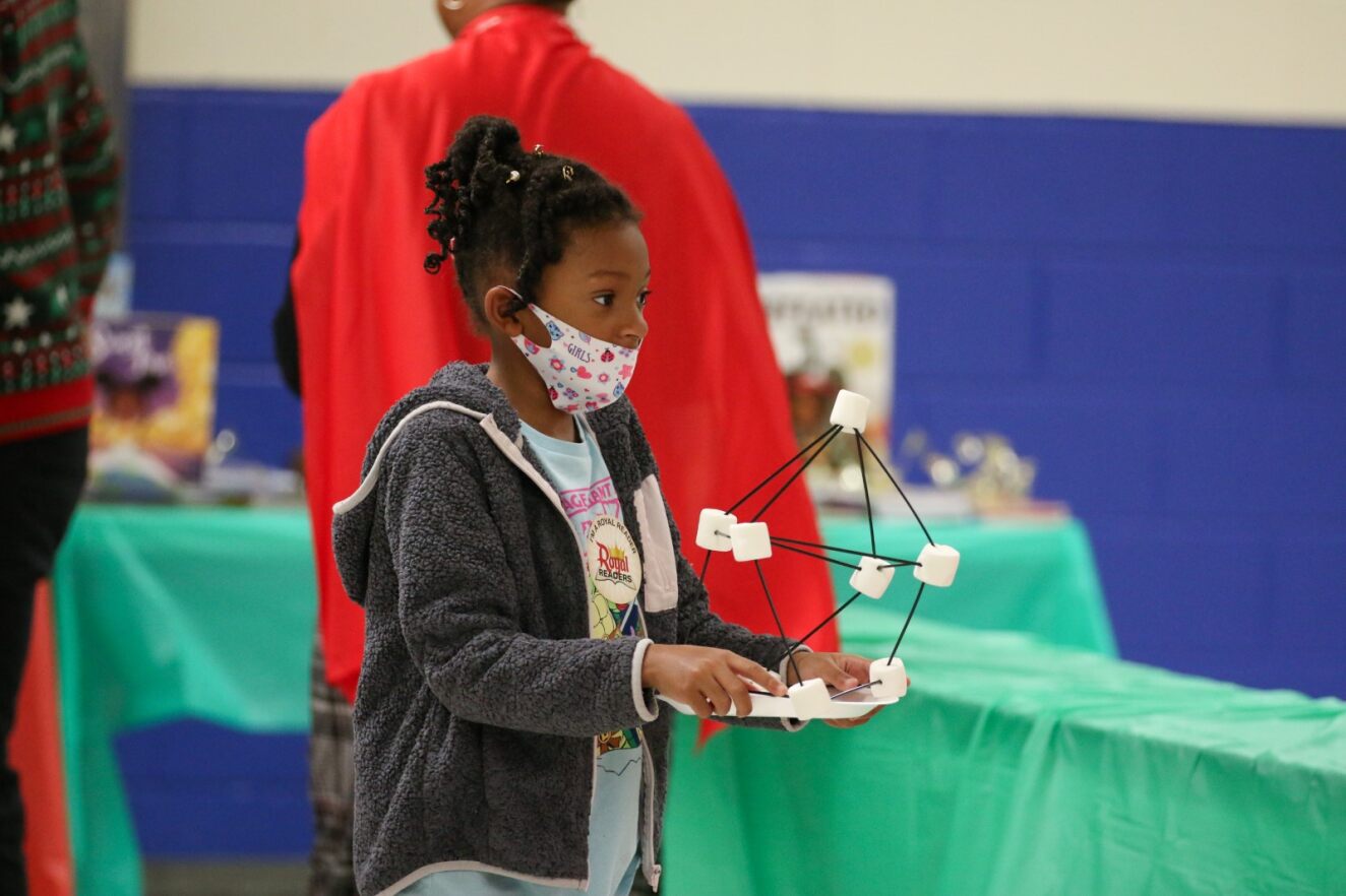 A young girl in a mask carries her marshmallow craft.