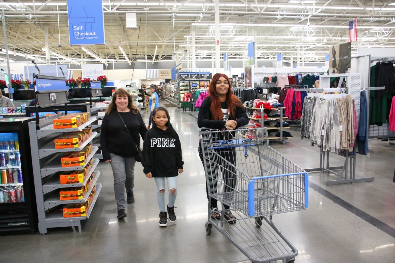 A girl and two women walk through Walmart with their cart.