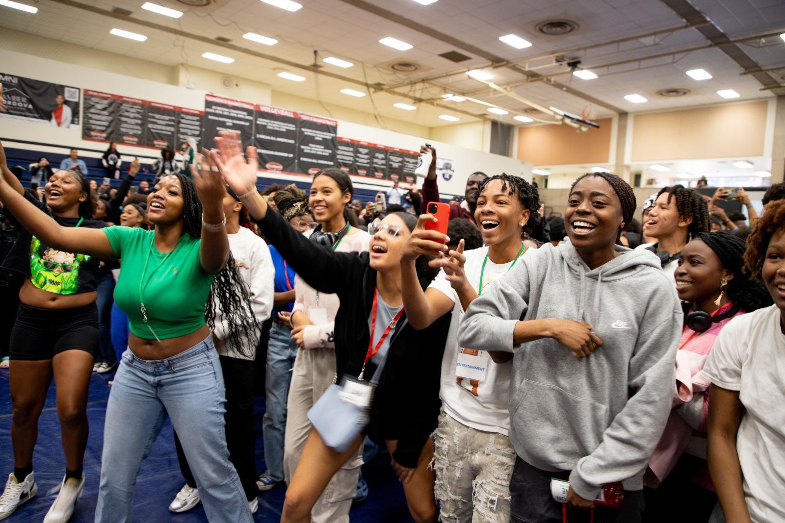 The crowd of students cheers while holding up their arms and phones.