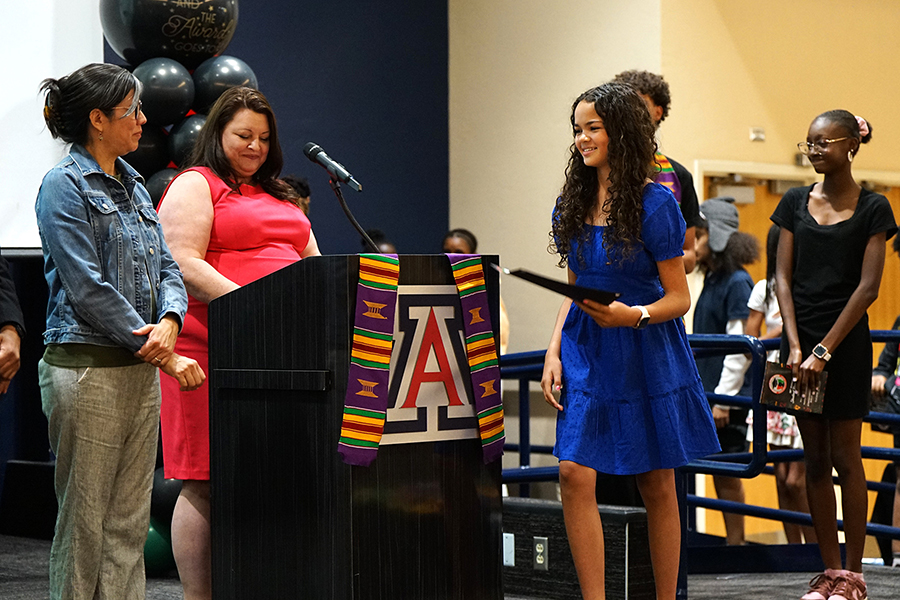 A girl in a blue dress smiles as she walks across the stage