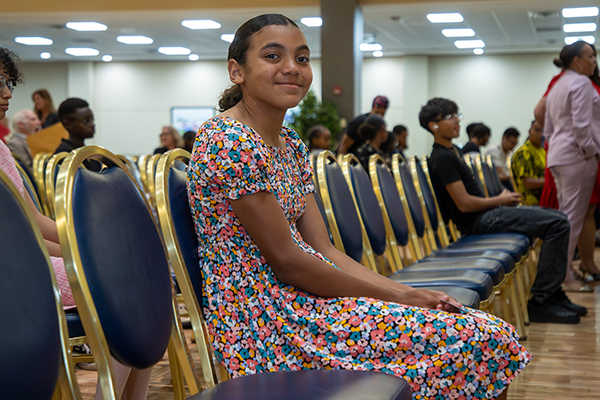A girl in a floral dress smiles in her seat