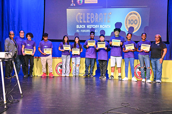 Students in purple shirts pose with their award plaques