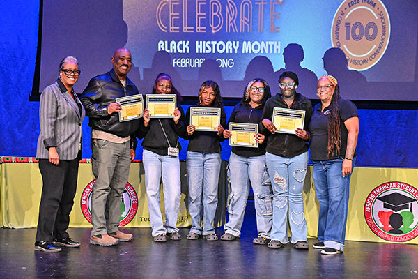 Students in black tops and jeans pose in a row with their award plaques