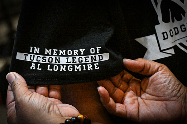 A man holds a hem of a black t-shirt printed with the words In Memory Tucson Legend Al Longmire