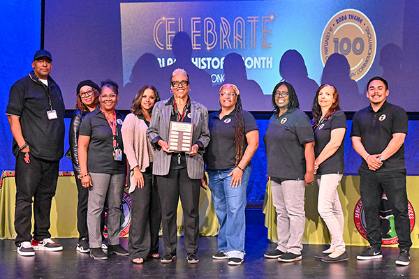 A group of staff members pose in front of a slideshow graphic