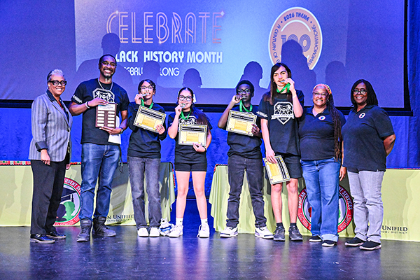 A group of students pose biting their medals and holding awards plaques