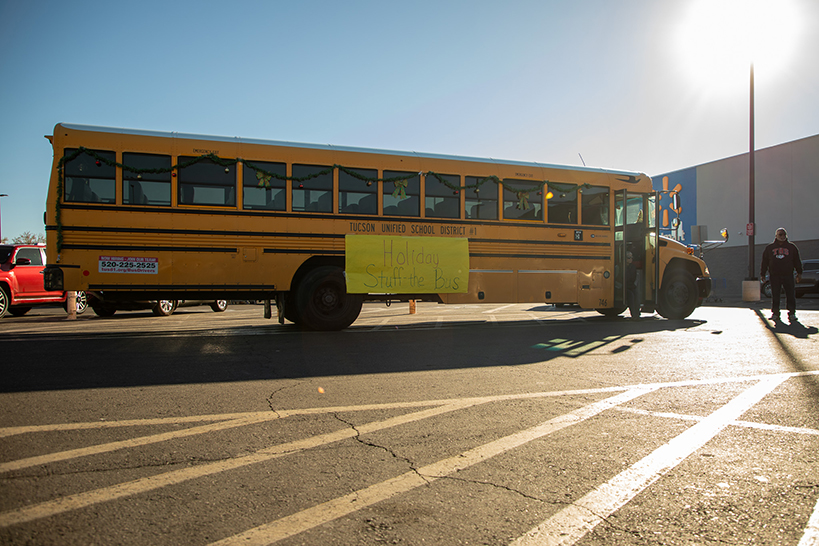 A school bus decorated with Christmas lights with a banner reading Holiday Stuff the Bus