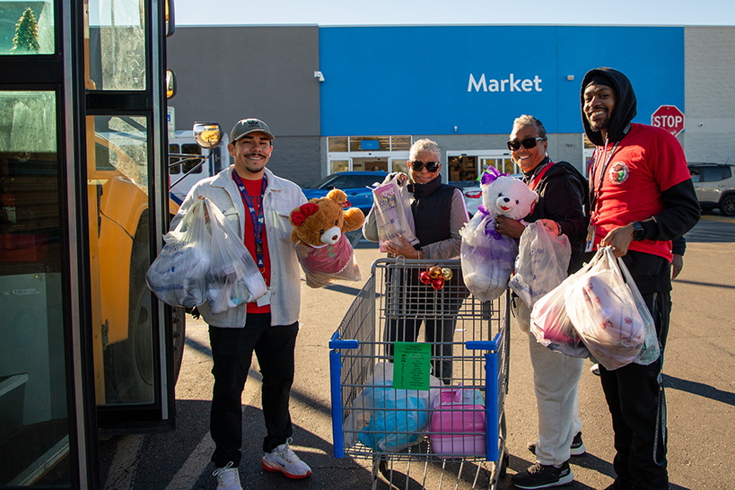 Four people stand outside the bus holding up bags of gifts