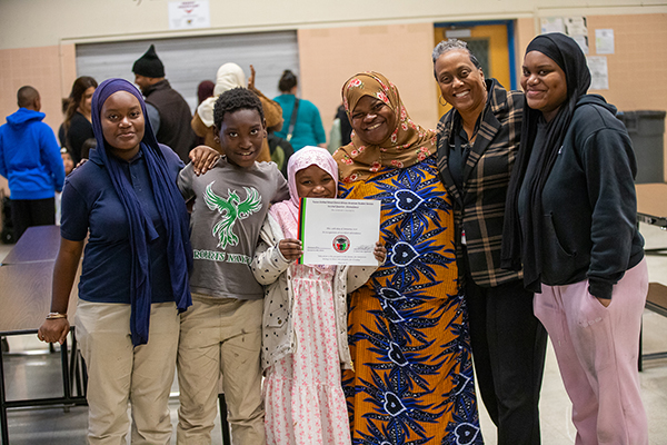 A little girl, center, holds up her award certificate surrounded by her siblings and family