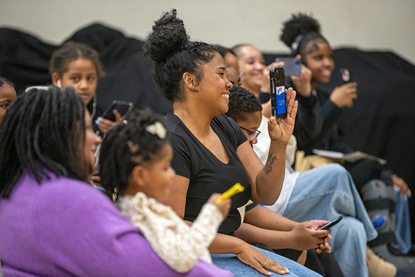 A mom proudly takes a photo of her child on stage with her phone