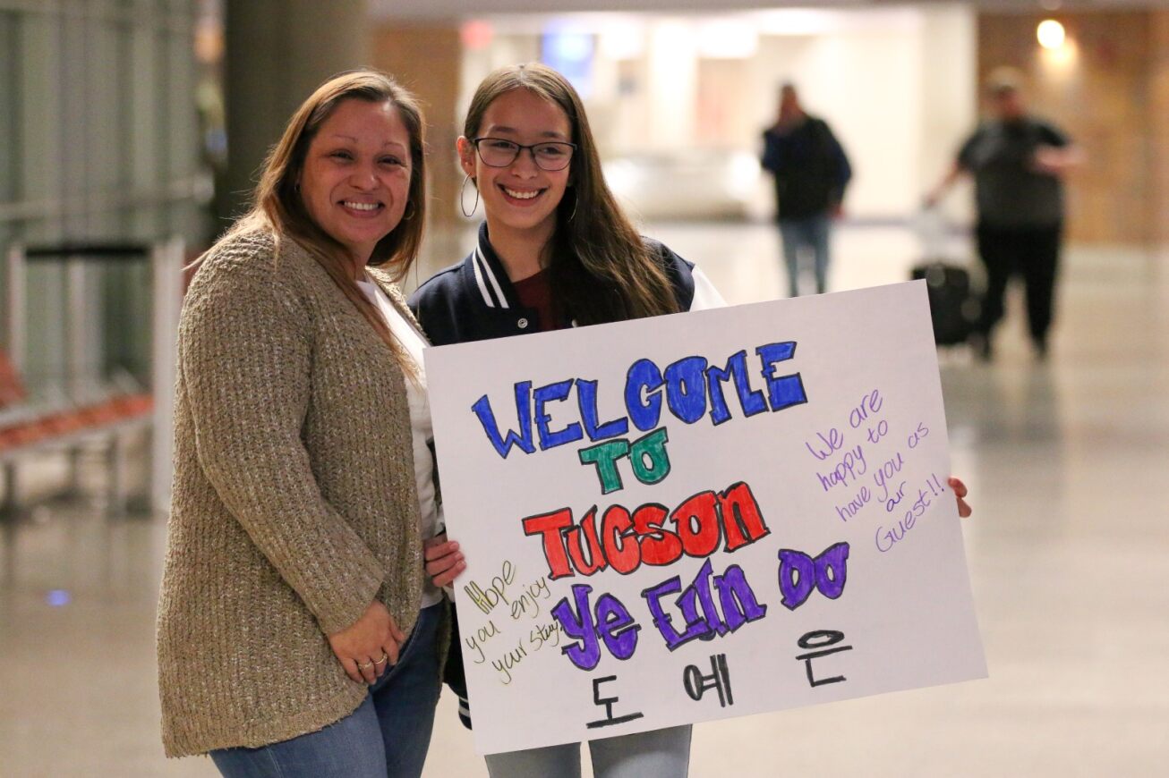 A host family holds up a sign for their TKAP student.