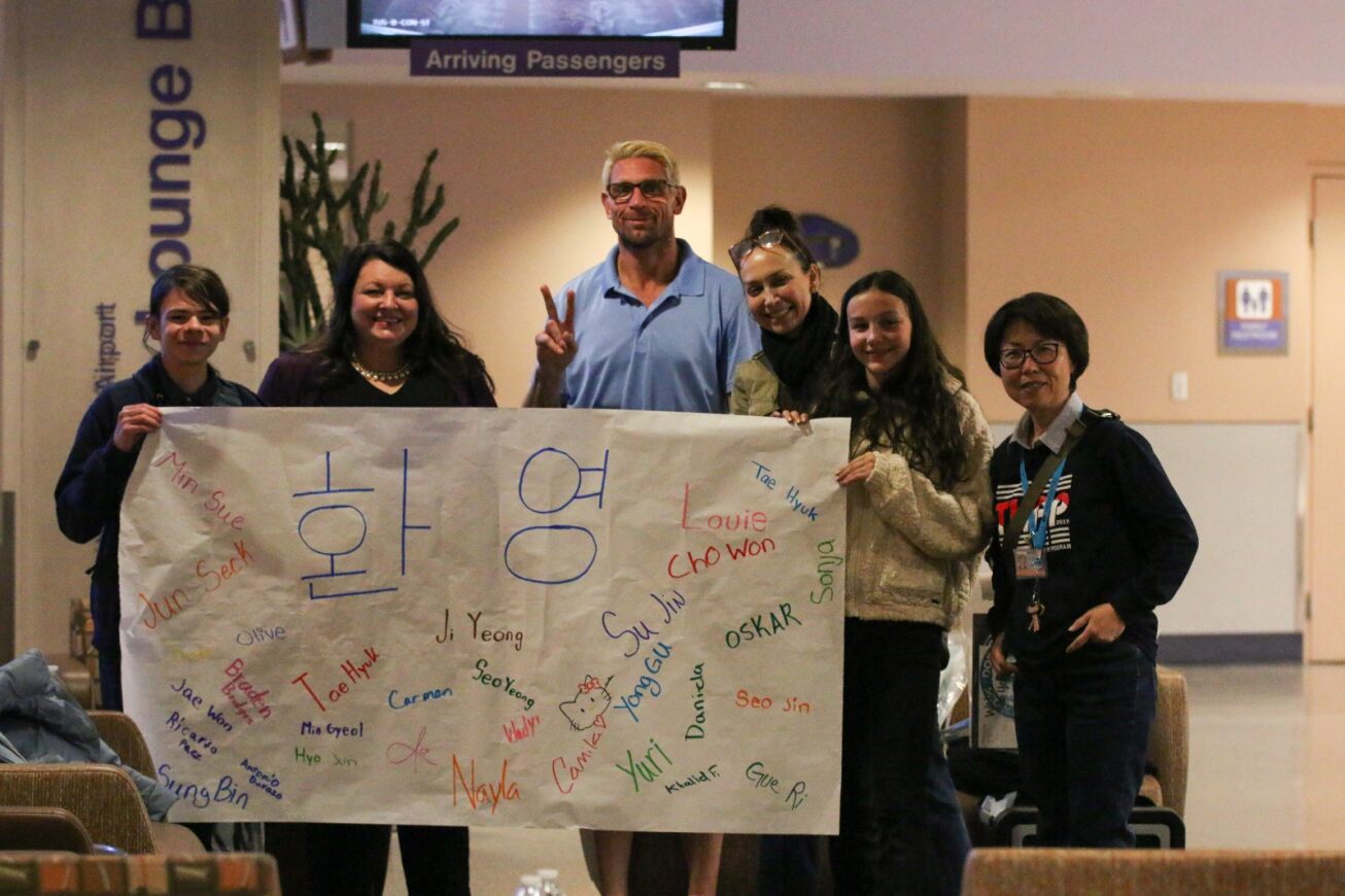 A host family holds up a banner welcoming their TKAP student.