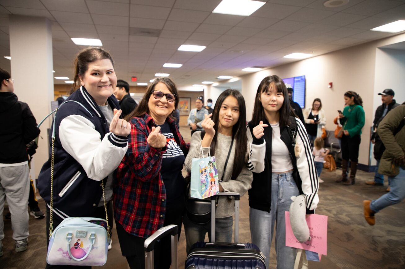 A host family and their Korean students make the Korean symbol for love with their fingers