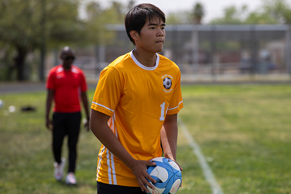 A teen boy in a yellow jersey holds the soccer ball