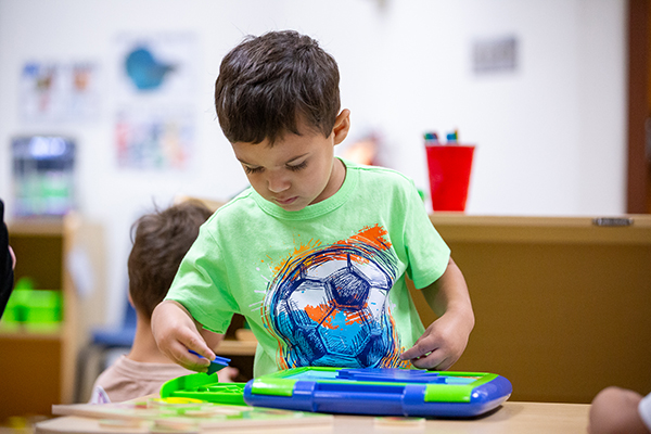 A little boy in a green shirt plays with tiles