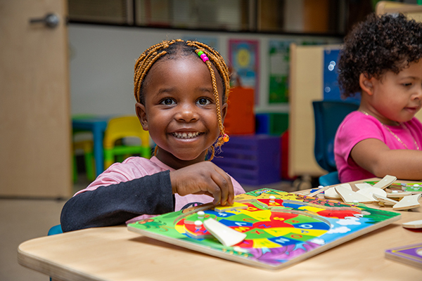 A little girl smiles as she plays with a colorful wooden board