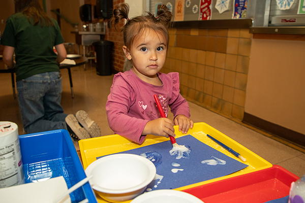 A little girl paints glue onto a piece of blue paper