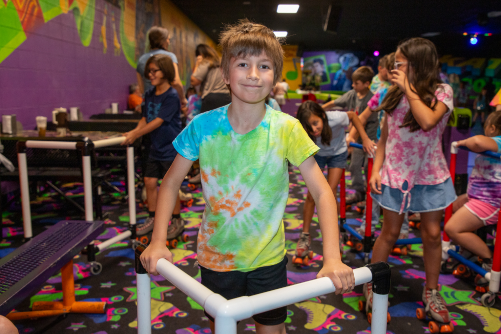 A boy in a tie-dye shirt smiles while holding a skate walker