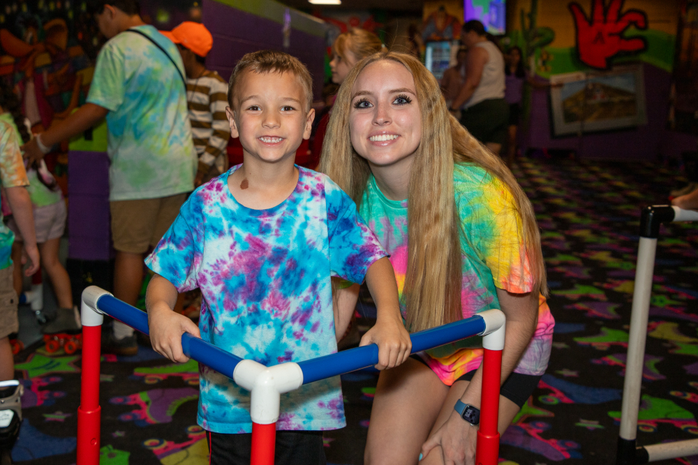 A boy and young woman in tie-dye shirts smile together