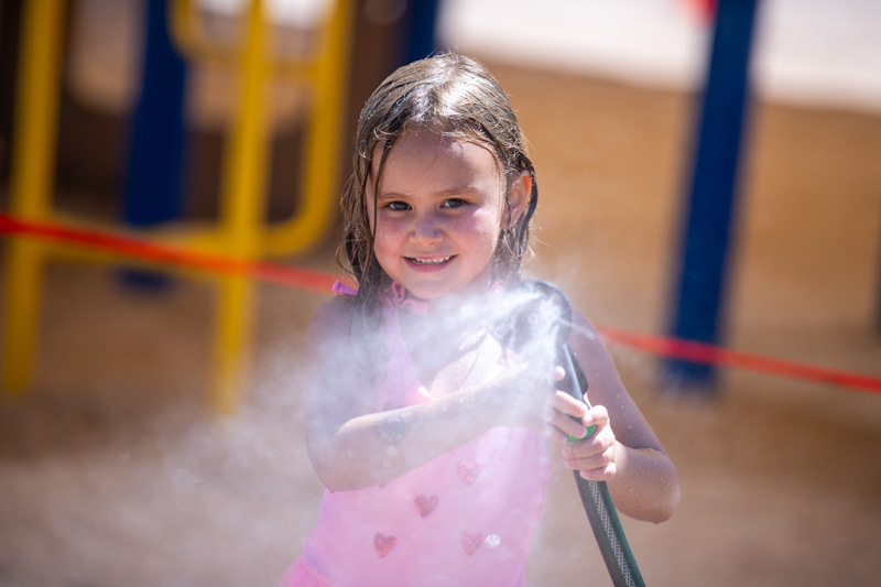 A little girl holds up a spraying water hose
