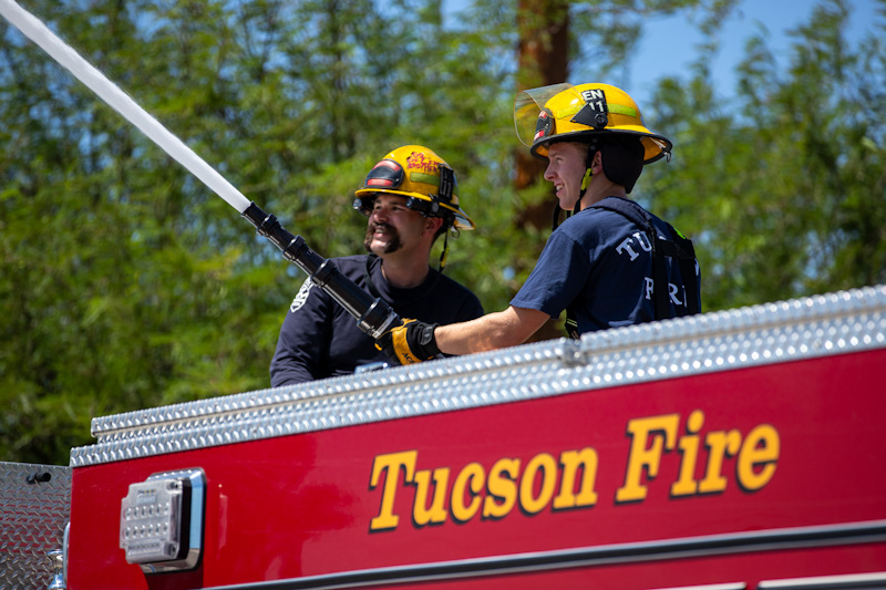 Two firefighters spray their hose from the fire truck