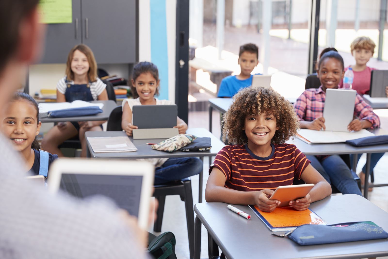 group of diverse smiling preteens in classroom looking at teacher