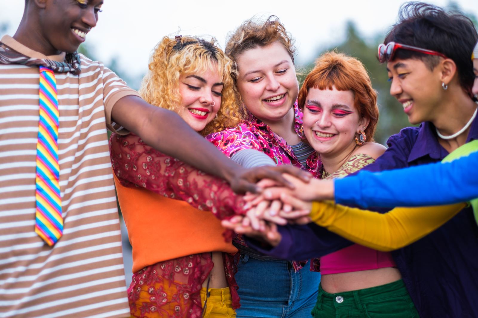 group of 5 teens stacking hands in unity, one wear a pink-yellow-blue striped tie representing the pansexual flag