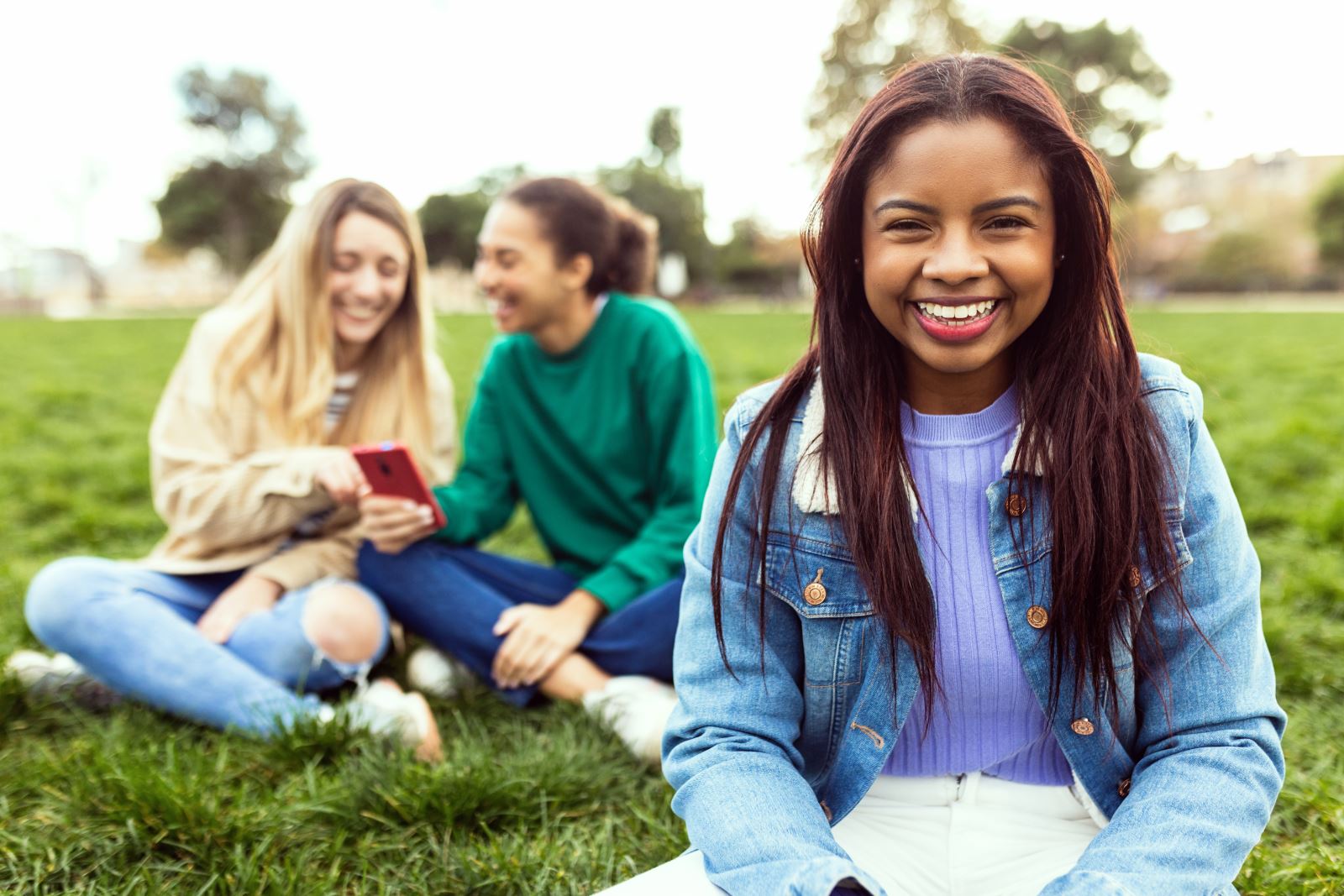 2 teen girls looking at a phone and smiling in background, 1 teen girl smiling in foreground