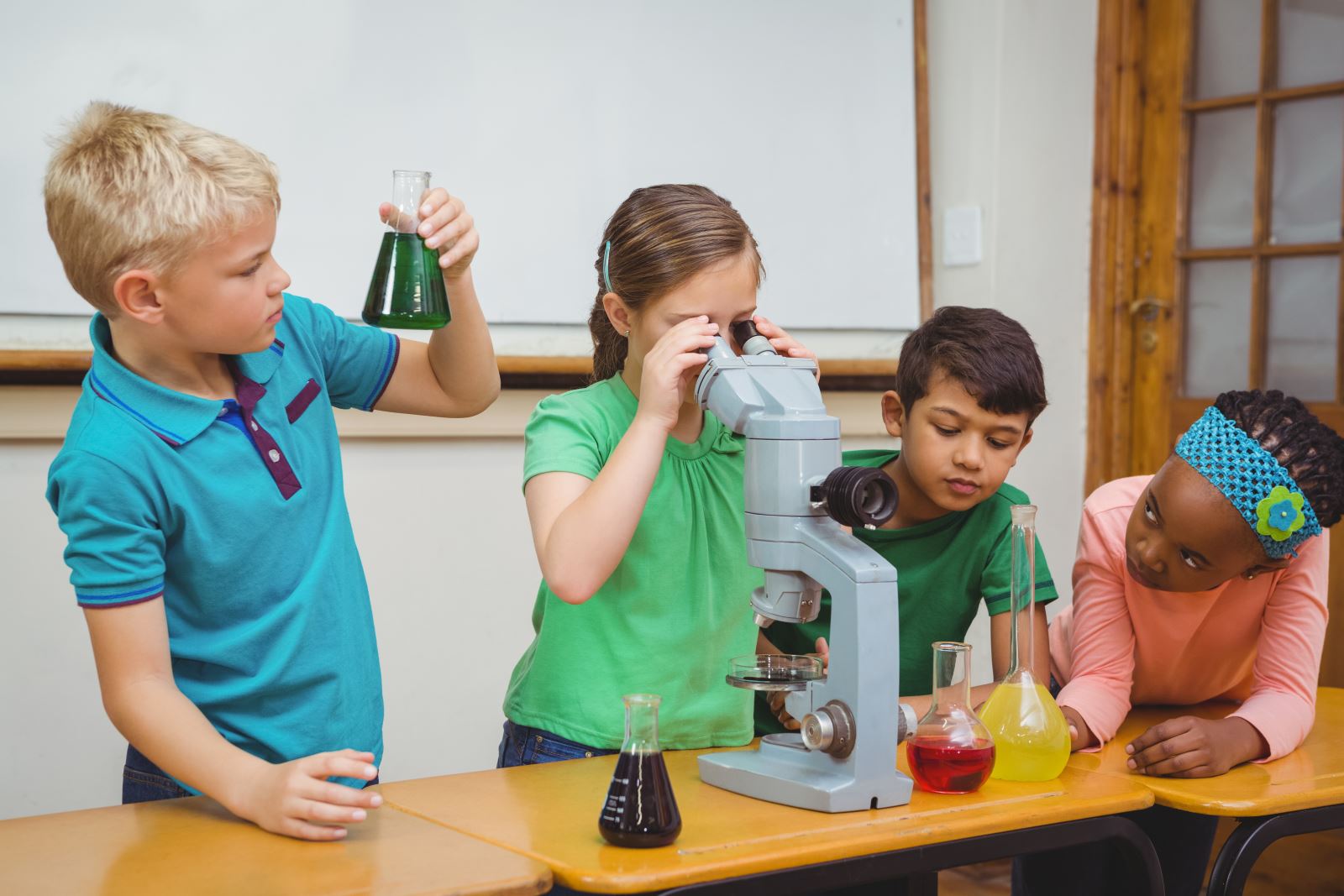 4 children explore science using a microscope and glass containers with various colored liquids