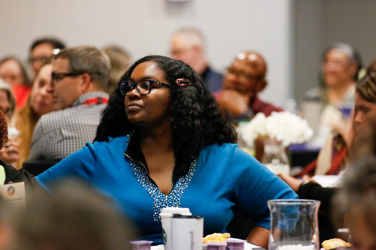 A woman in a blue shirt listens to a presentation.