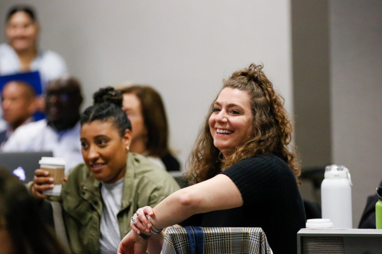 Two women smile while listening to a presentation