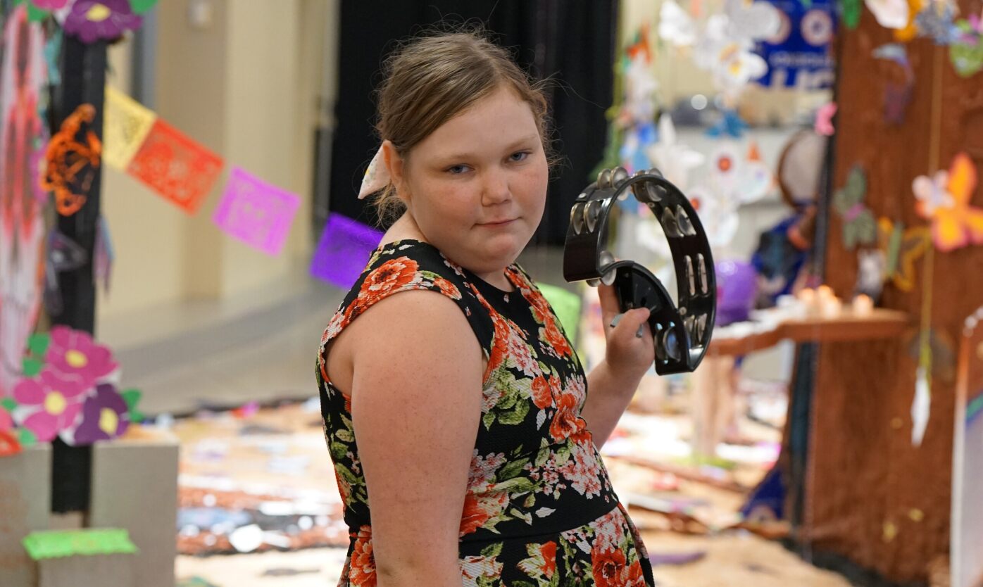 A girl plays the tambourine in a floral dress. 