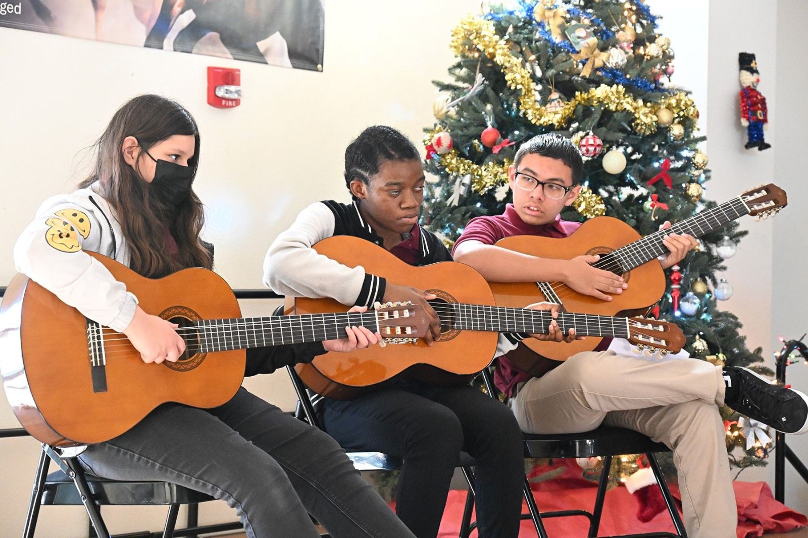 Three students play Christmas songs on the acoustic guitar.