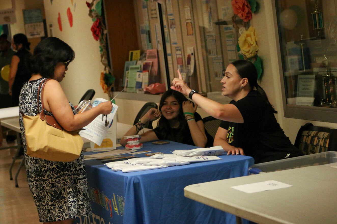 Woman checks out table staffed by a student and employee at the Catalina Family Mixer.