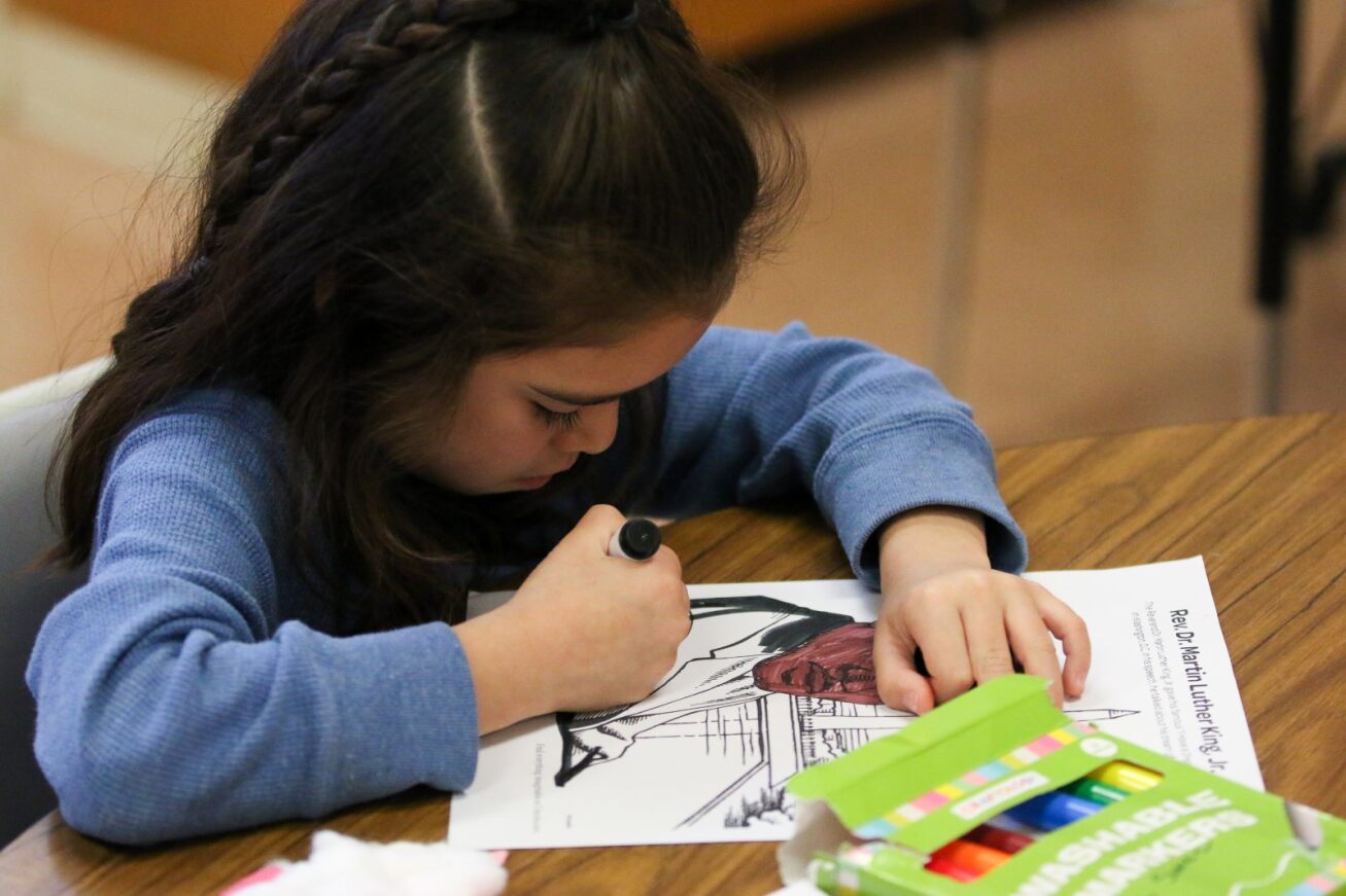 A girl colors in an MLK Jr. coloring page.
