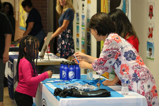 Child receives pen from table staffed by 2 employees.