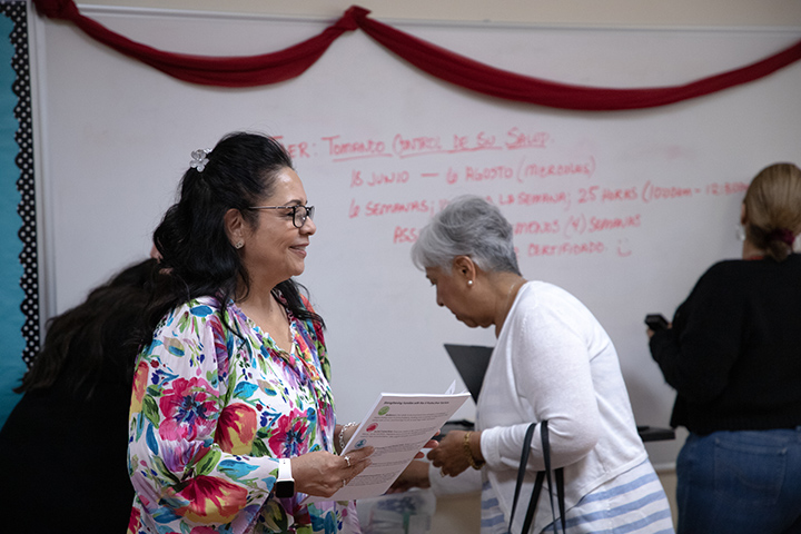 A woman in a floral shirt holds a stack of papers