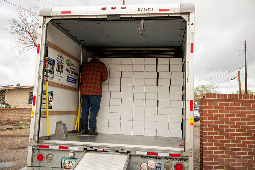 A man stands in the back of a truck unloading white boxes