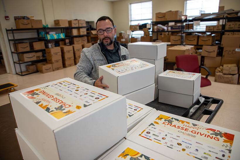 A man with a beard and glasses picks up a stack of white boxes from a table