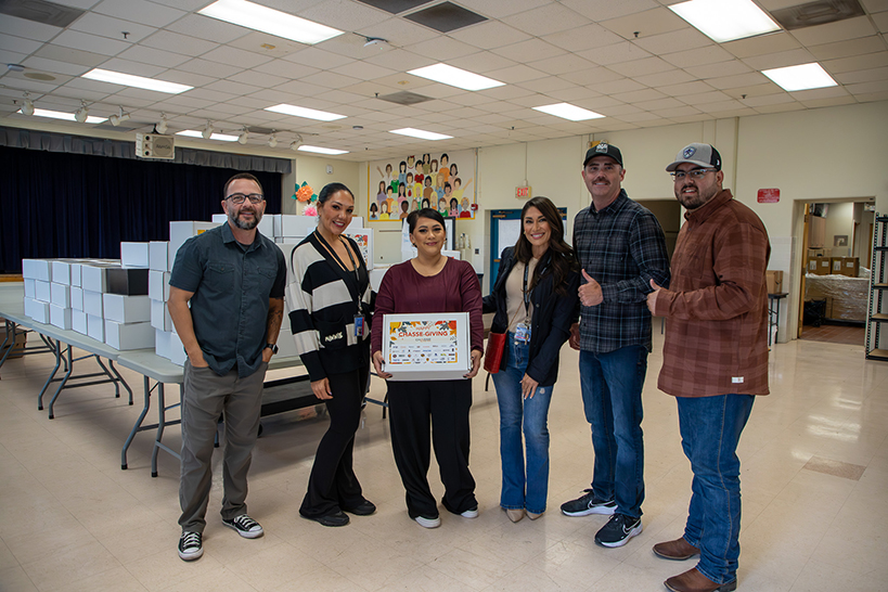 Six people pose for a photo, with a woman in the middle holding a white Giving Box