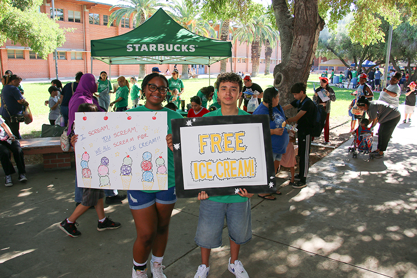 A teen girl and boy smile while holding posters advertising free ice cream