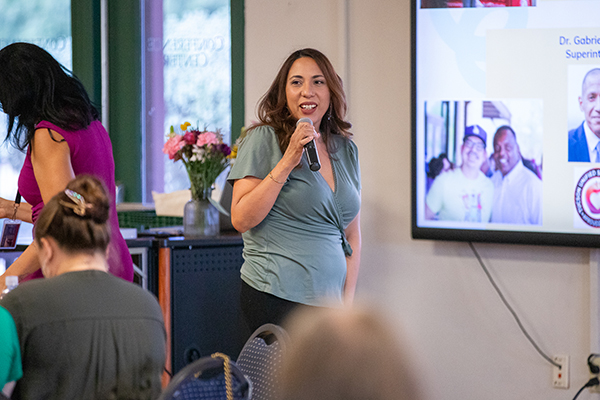 A woman talks into a microphone to the crowd at a luncheon