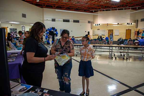 A woman talks to a mom and her daughter at a table in the cafeteria