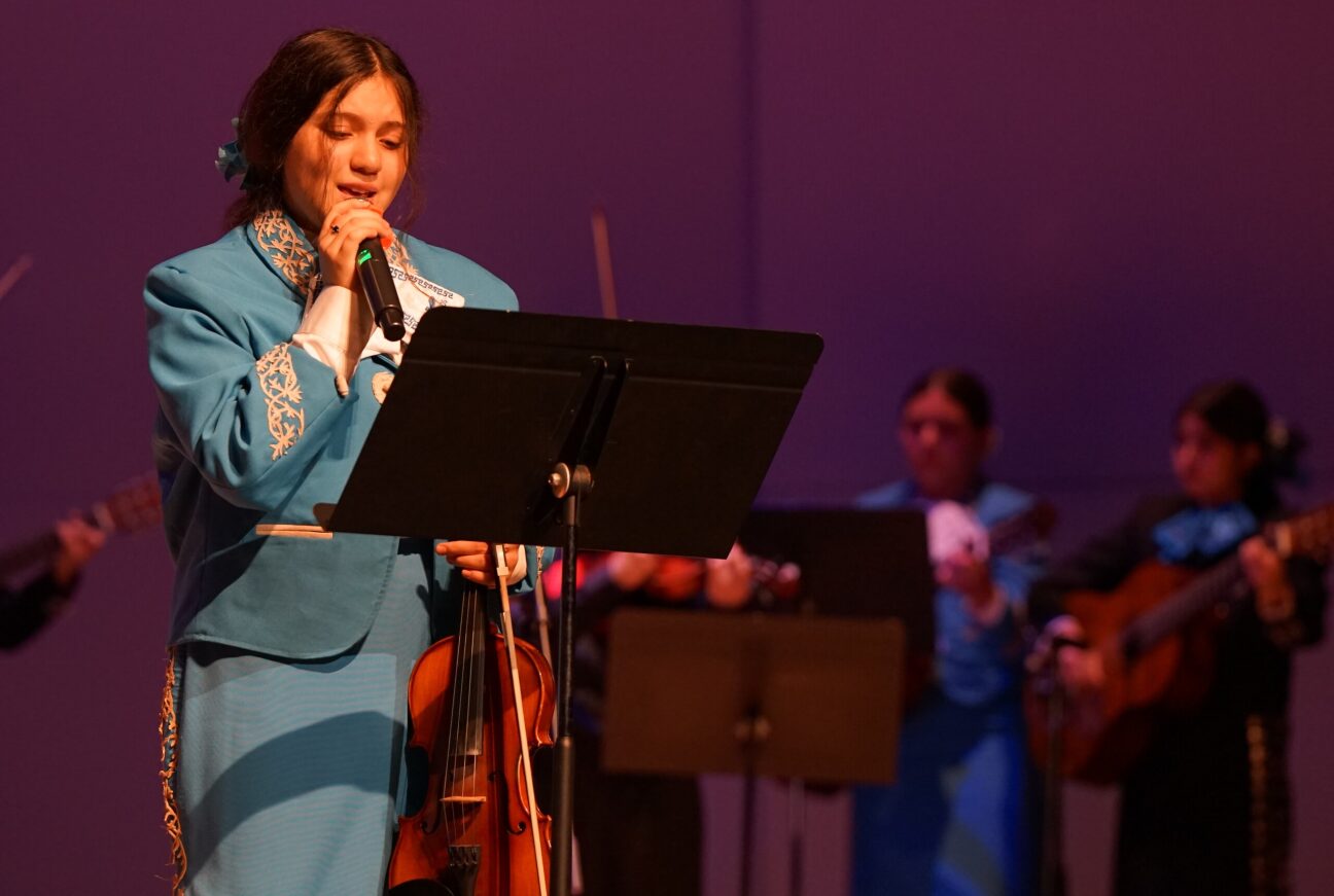 A student performs her solo in front of the crowd, holding a mic and violin