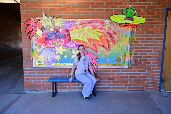 A woman sits on a bench in front of her students' colorful mural